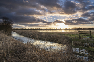 Sunrise and cloudy skies over flooded wetland with stream in foreground