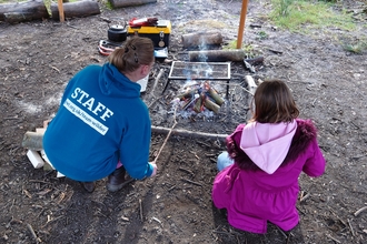 Staff member showing a child how to use a campsfire safely