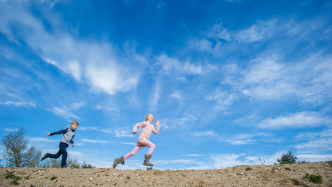 Two children run across a beach with a blue sky above