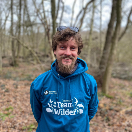 Man in teal #TeamWilder hoodie stood in woodland smiling facing the camera