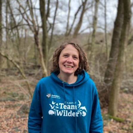 Woman in teal #TeamWilder hoodie stood in woodland smiling facing the camera