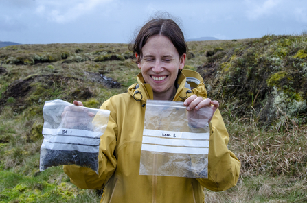 Jo holding up two sample bags: one full from a control plot of bare peat; and a second from a a plot that had been treated with PeatFix