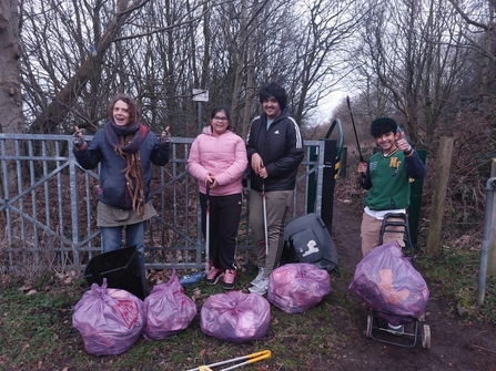 Group of youths having sone a litter pick, posing for the camera with 5 full bags of rubbish collected on the ground in front of them. It's an autumn day as they have warm coats and hats on.