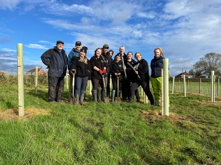 Group of people out on a nature reserve gathered for a group shots holding their tools ready to start planting a hedgerow. It's a lovely day in winter.