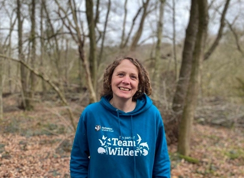 Woman in teal #TeamWilder hoodie stood in woodland smiling facing the camera