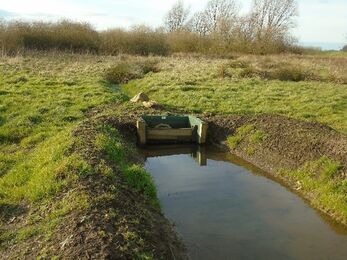 A small wooden sluice sits between two green banks with water held back in the foreground