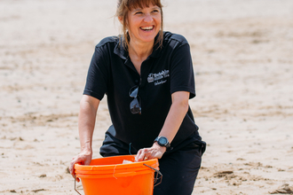 Emma Dawber, volunteer, smiling on beach with orange bucket