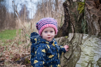 Poppy the toddler stands next to a tree stump