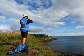 Man surveying for cetaceans with binoculars on a cliff top