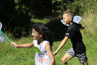 Two children running in the sunshine with butterfly nets