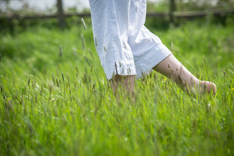 A person wearing white trousers walks barefoot in grass