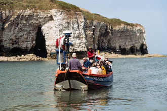 Rear view of people on a boat departing out to sea on a wildlife watching cruise in a coble boat