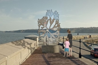 A metal seaweed sculpture positioned on the end of a harbour looking out to sea.
