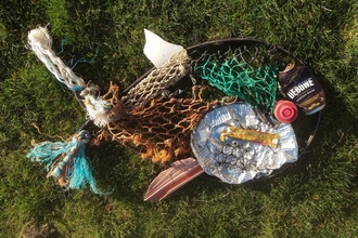 Marine litter arranged into the shape of a fish including nets and crisp packets