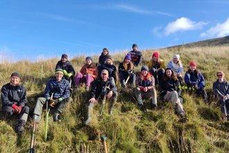 group of people sat on the side of the mountaintop after completing some tree planting