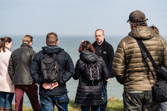Image showing a person giving a talk to a group of people. The sea is in the background.