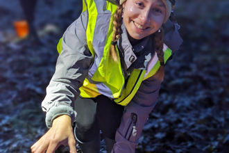 A smiling woman in high vis looks at the camera, holding out a crab