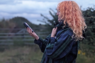 A young woman with pink hair holds out a bat detector