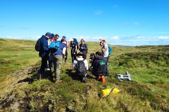 A group of people on top of a small hill, looking at something in front of them with a blue sky above.