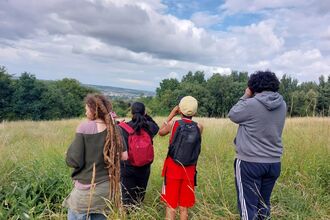 A group of young people outdoors with a adult. Looking for birds with binoculars