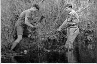 Two men are working together in the water, using shovels to complete their task.