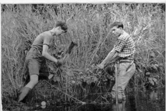 Two men are working together in the water, using shovels to complete their task.