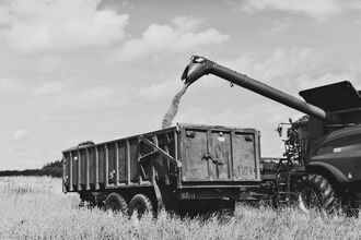 Black and white image showing a tractor harvesting a field