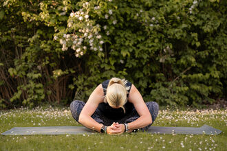 A woman sits in child's pose on a Yoga mat in a flowery medow