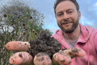 A man holding out his palm to the camera with a heap of peat-free compost on it stood in a wild garden.