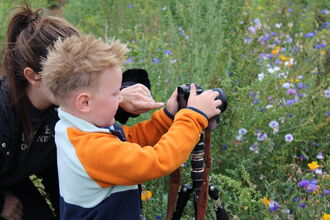 A lady helps a young boy take a photo of wildflowers
