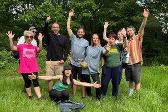 Group pose for photo smiling with arms out in the outdoors after event
