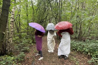 three people dressed as mushrooms stand in a forest 