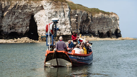 Rear view of people on a boat departing out to sea on a wildlife watching cruise in a coble boat