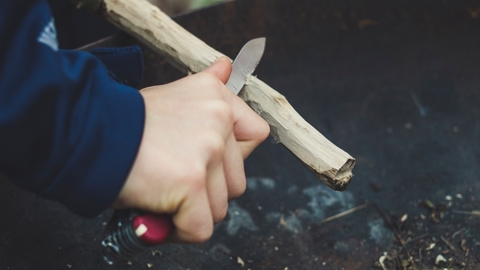 Hand with whittling knife working on a piece of wood