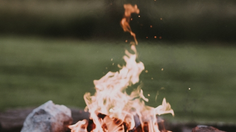 Photo of campfire comprised of stones and wood with blurred background of grass