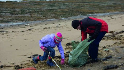 An adult and a child clean the strandline on a sandy beach with a litter picker