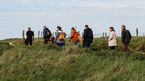 A group of people on a guided walk, following a leader on a path.