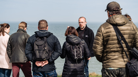 Image showing a person giving a talk to a group of people. The sea is in the background.