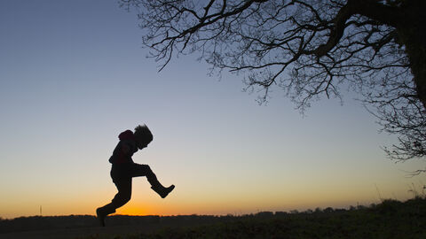 A silhouette of a child playing outdoors at sunset, The Wildlife Trusts