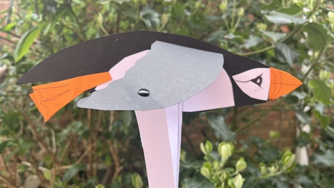 Paper puffin puppet with flapping wings in front of a leafy bush