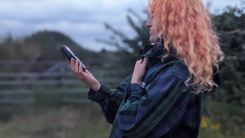 A young woman with pink hair holds out a bat detector