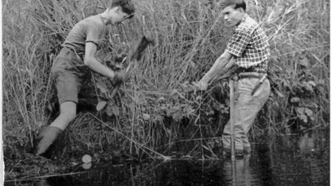 Two men are working together in the water, using shovels to complete their task.