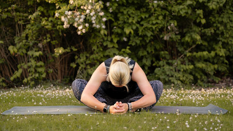 A woman sits in child's pose on a Yoga mat in a flowery medow