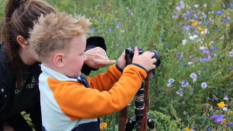 A lady helps a young boy take a photo of wildflowers