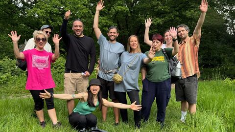 Group pose for photo smiling with arms out in the outdoors after event