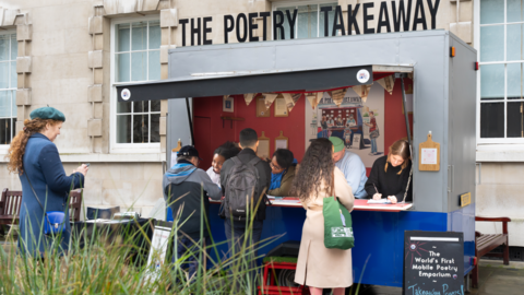Customers gather outside a converted takeaway bus as poets writ on paper.