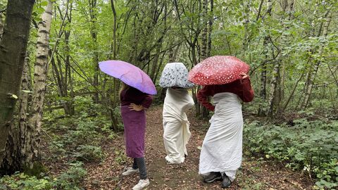 three people dressed as mushrooms stand in a forest 
