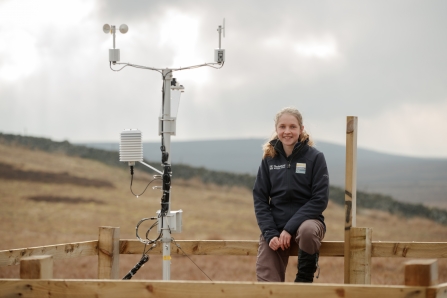 Volunteer sitting on fence next to weather station