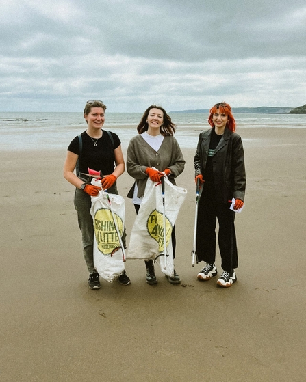 Three women stood facing the camera on a beach with litter picking bags