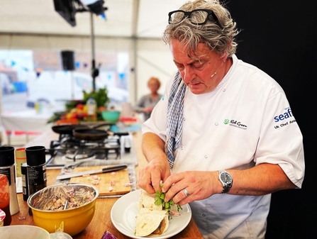 Chef Rob Green doing a cookery demonstration. He's folding a wrap and has a bowl of ingredients and other condiments in front of hm